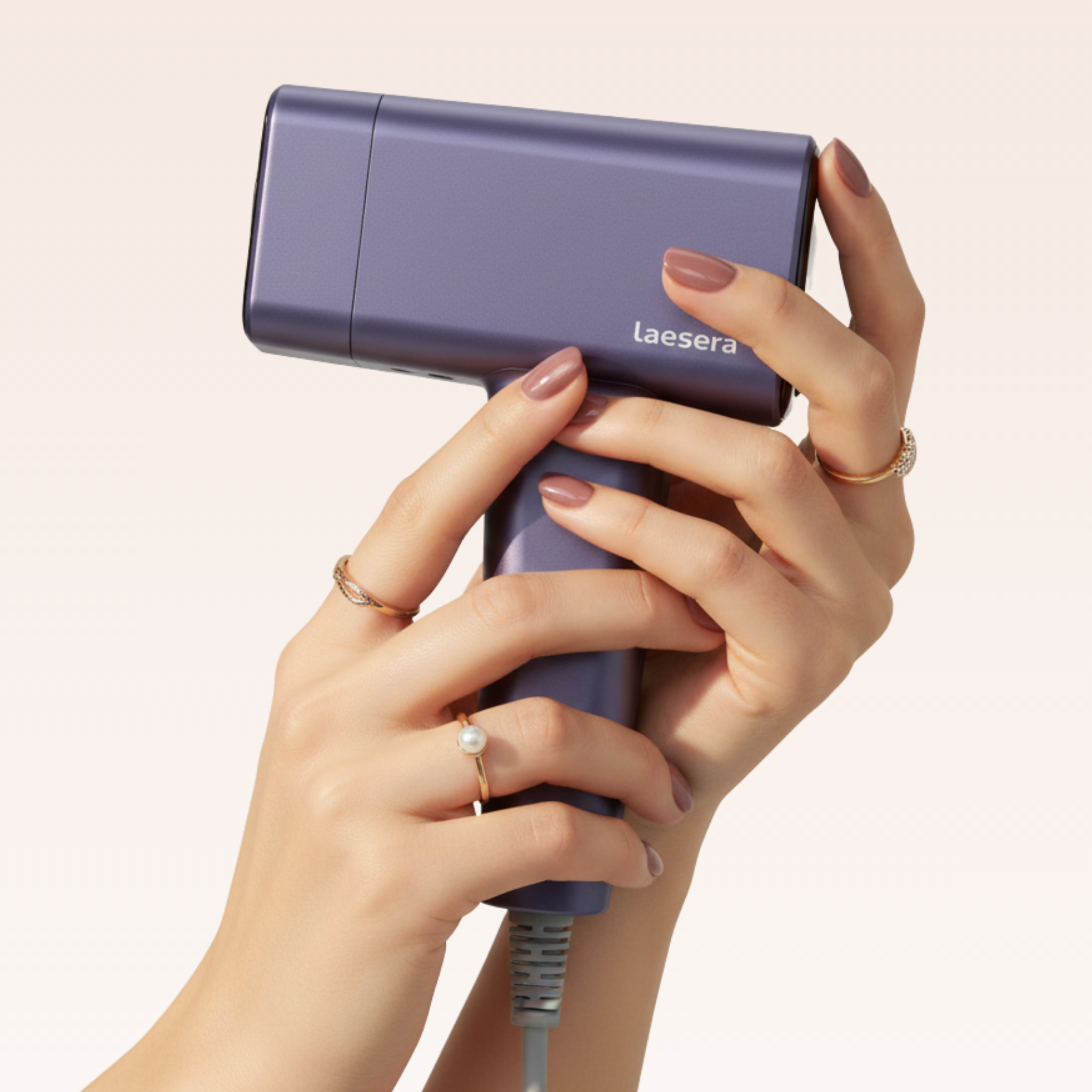 Close-up van de Laesera Nova One IPL vastgehouden door verzorgde handen met gouden sieraden.